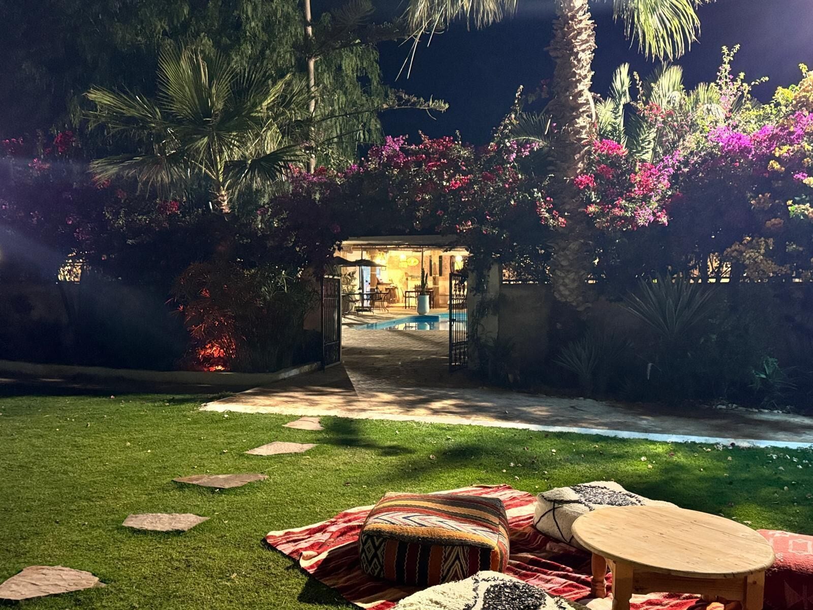 Ein gut beleuchteter Garten mit Pool, Sitzgelegenheiten im Freien und einem Weg zu einem Gebäude.
