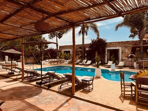 A pool area with lounge chairs, a table, and a stone building in the background.