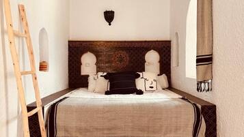 A bedroom with a wooden ladder, a patterned rug, and a bed with two pillows and a black pillow.