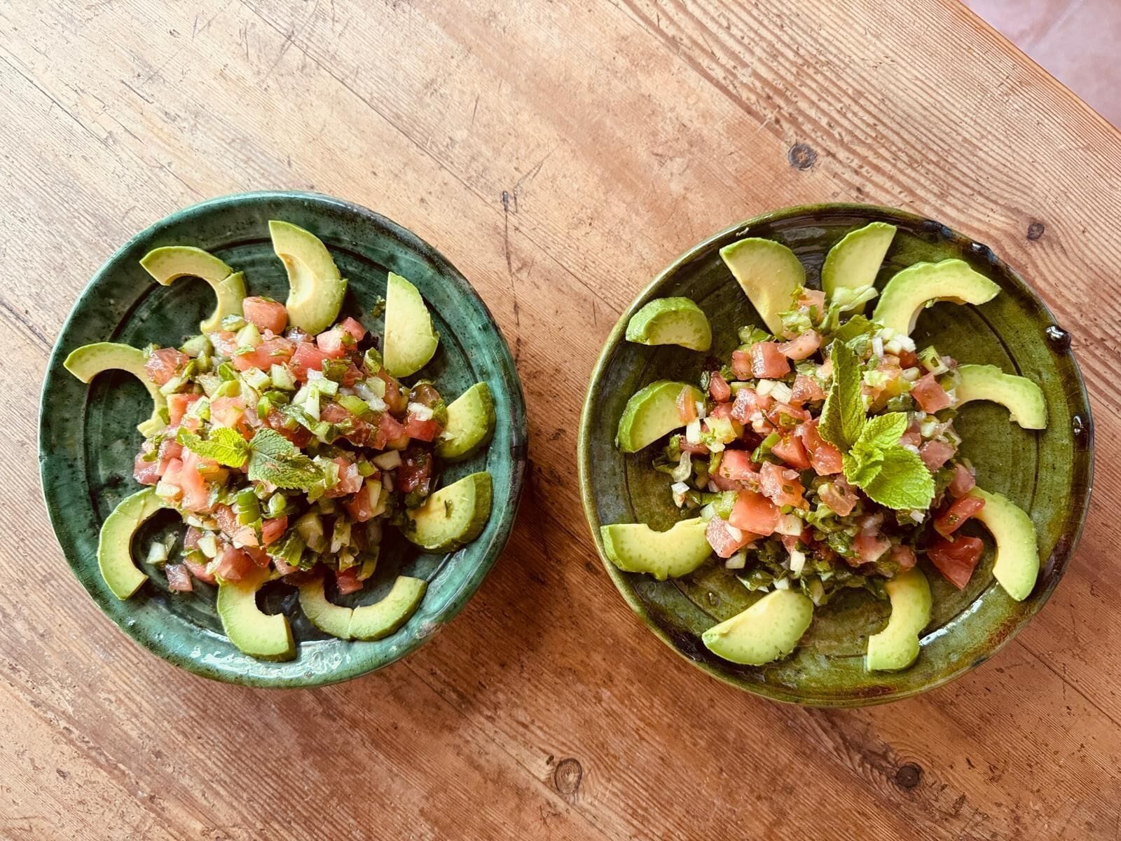 Two bowls of avocado and tomato salad on a wooden table.