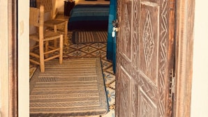 A traditional room with a patterned rug, a bed with blue bedding, a woven chair, and a decorative door. - RIAD EUCALYPTUS, ETHNIC HOTEL (Essaouira)
