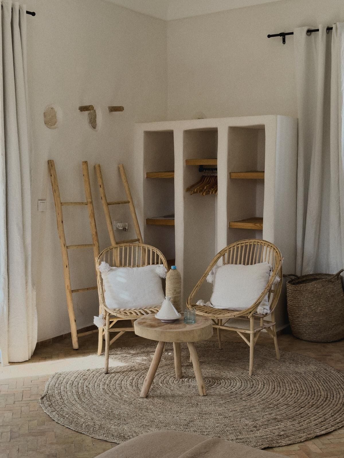 Une pièce comprenant deux fauteuils en osier, une petite table ronde et un meuble de rangement blanc avec des étagères.