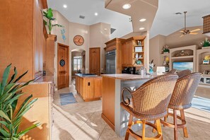 A spacious kitchen with wooden cabinets, a central island, and a dining area with wicker chairs. - Intervillas Florida - Villa Valentina (Cape Coral)