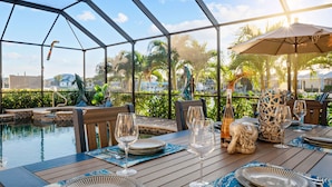 A dining area with a pool view, wooden tables, and outdoor seating. - Intervillas Florida - Villa Valentina (Cape Coral)