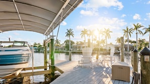 A wooden dock with a covered seating area, a boat, and palm trees in the background. - Intervillas Florida - Villa Valentina (Cape Coral)