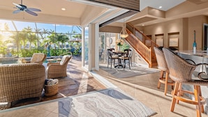 A spacious indoor area with wicker furniture, a dining table, and a staircase leading to an upper level. - Intervillas Florida - Villa Valentina (Cape Coral)
