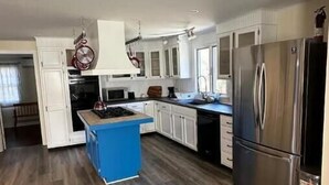 A modern kitchen with white cabinets, a blue island, stainless steel appliances, and a wooden floor.