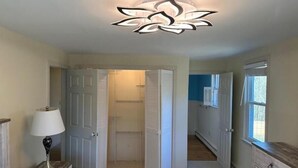 A bedroom with a bed, nightstand, lamp, and a ceiling light fixture.