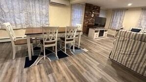 A living room with a dining table, chairs, a sofa, a TV, and a brick wall.