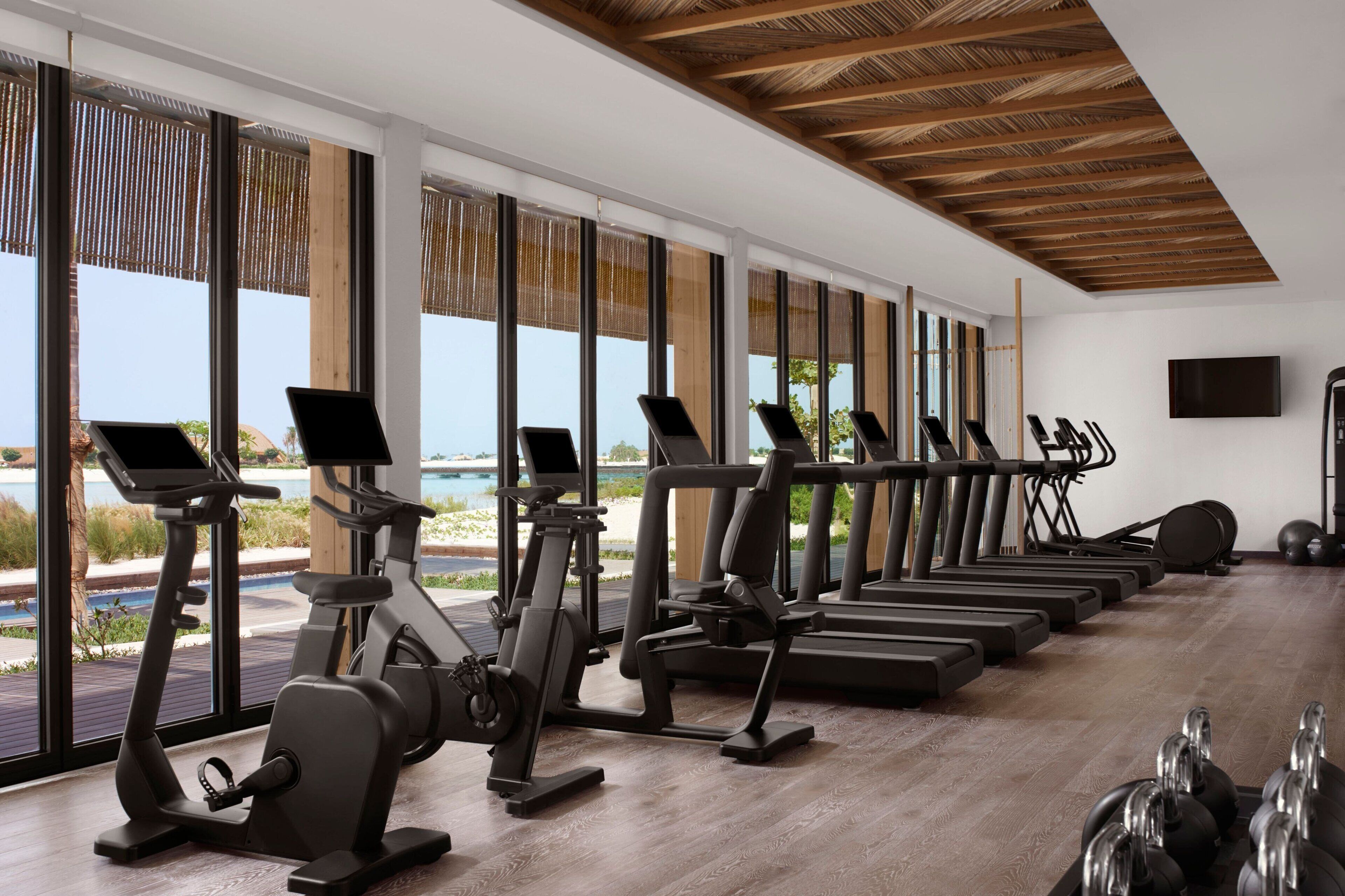 A gym with exercise equipment and large windows overlooking a pool.