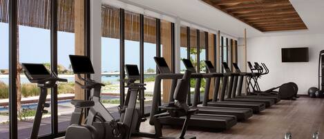 A gym with exercise equipment and large windows overlooking a pool.