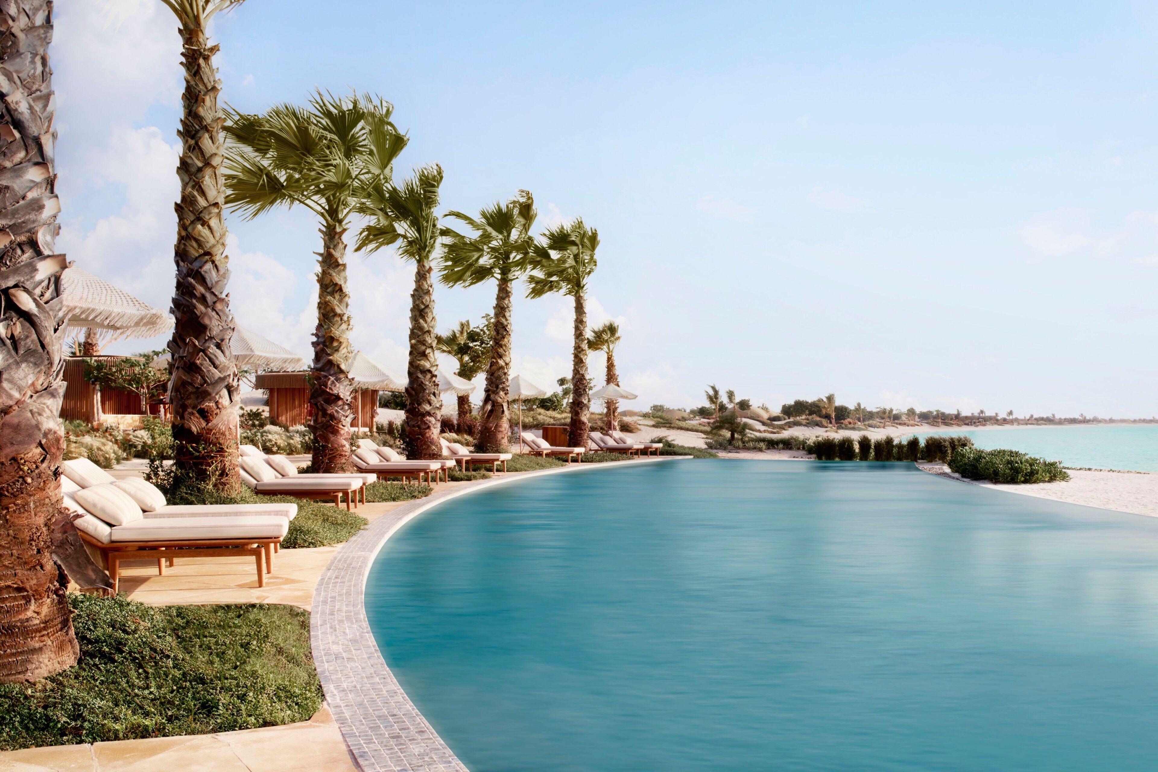 A poolside area with lounge chairs and palm trees, surrounded by a clear blue sky.