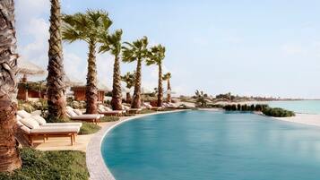 A poolside area with lounge chairs and palm trees, surrounded by a clear blue sky.