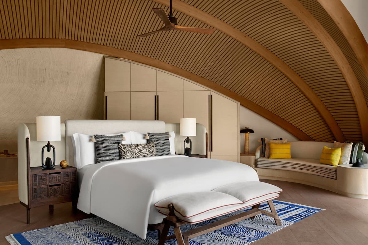 A bedroom with a large bed, two bedside tables, a bench, a sofa, and a ceiling fan.
