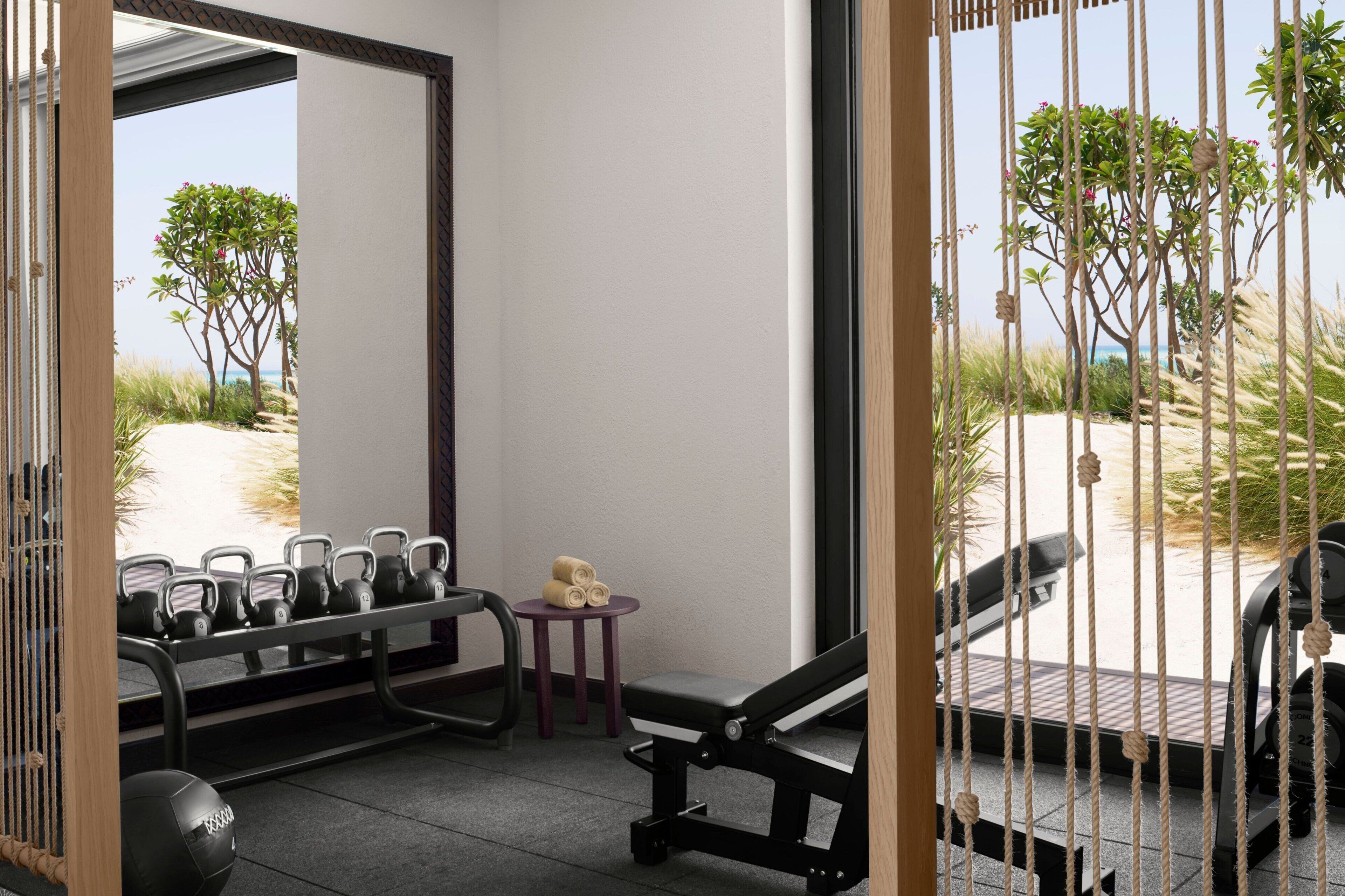 Une salle de sport équipée de matériel d’exercice, une petite table avec des serviettes et une vue sur la plage grâce à un grand miroir.