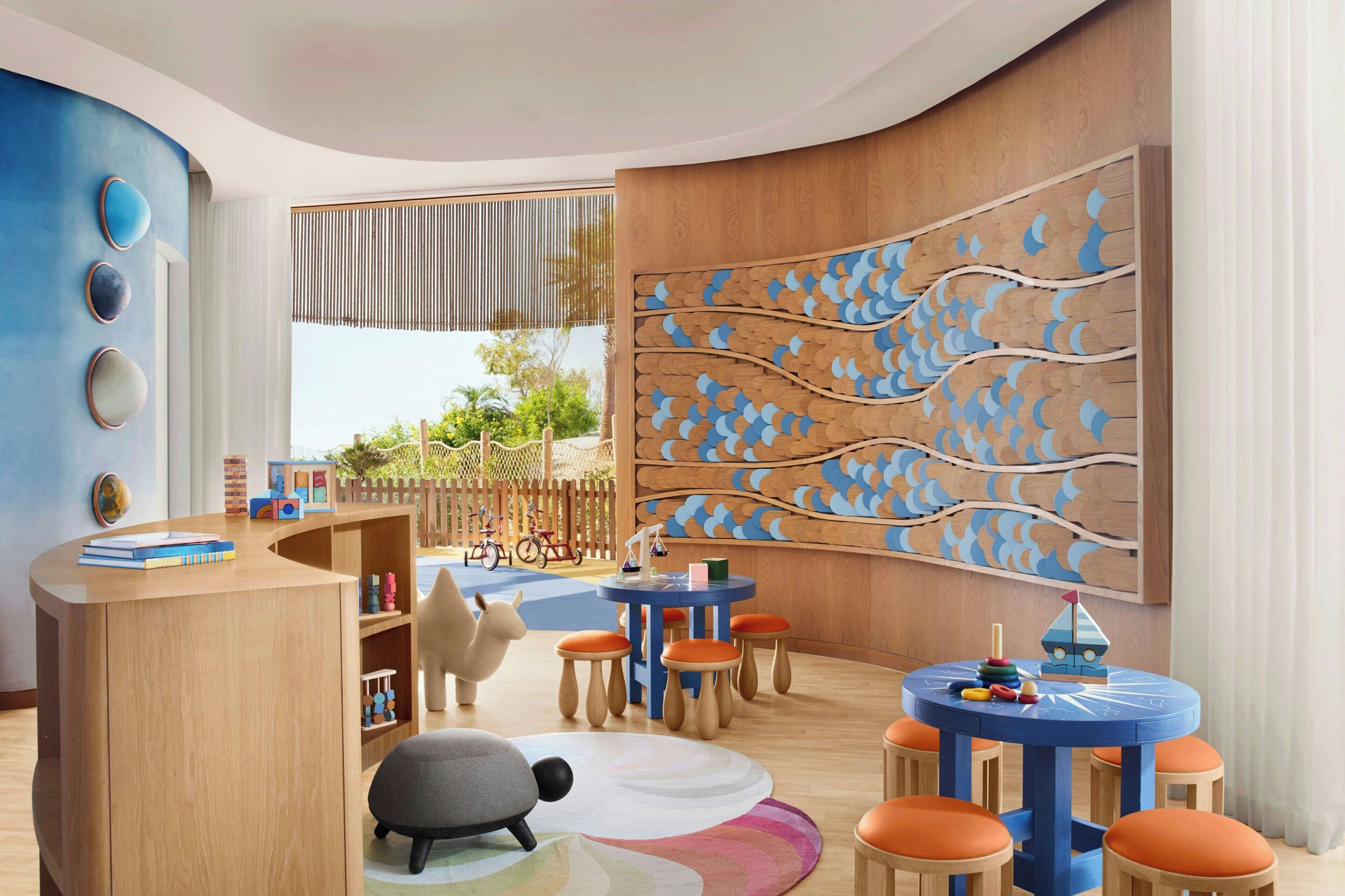 Un cuarto de juegos para niños con un escritorio de madera, sillas coloridas y un gran mural en la pared.