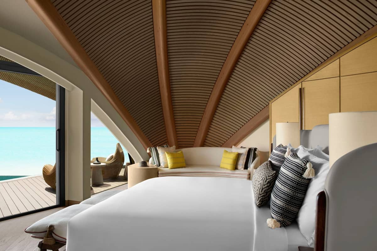 A bedroom with a large bed, wooden ceiling, and a view of the ocean.