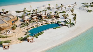 An aerial view of a resort with a large pool, sun loungers, and palm trees. - Nujuma, A Ritz-Carlton Reserve (Umluj)