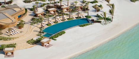 Vue aérienne d’un complexe hôtelier doté d’une grande piscine, de chaises longues et de palmiers.