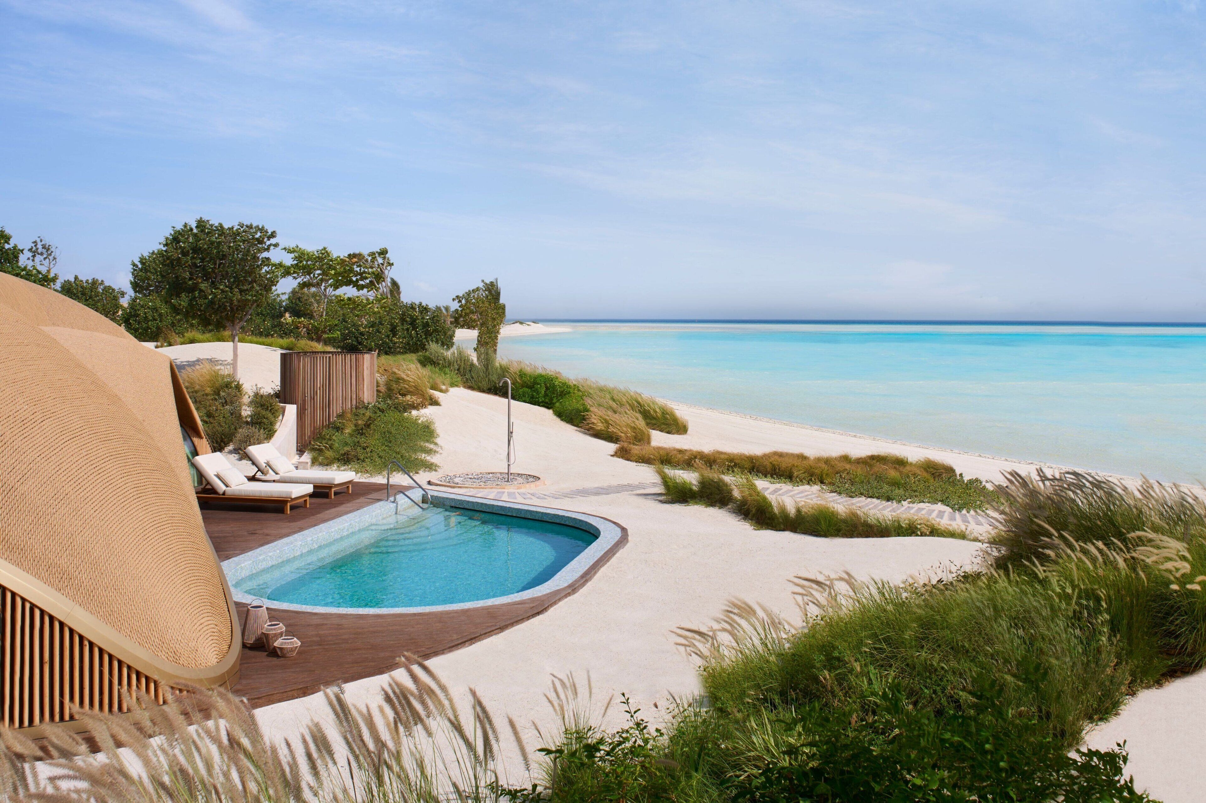 A poolside area with lounge chairs, a pool, and a beach view.