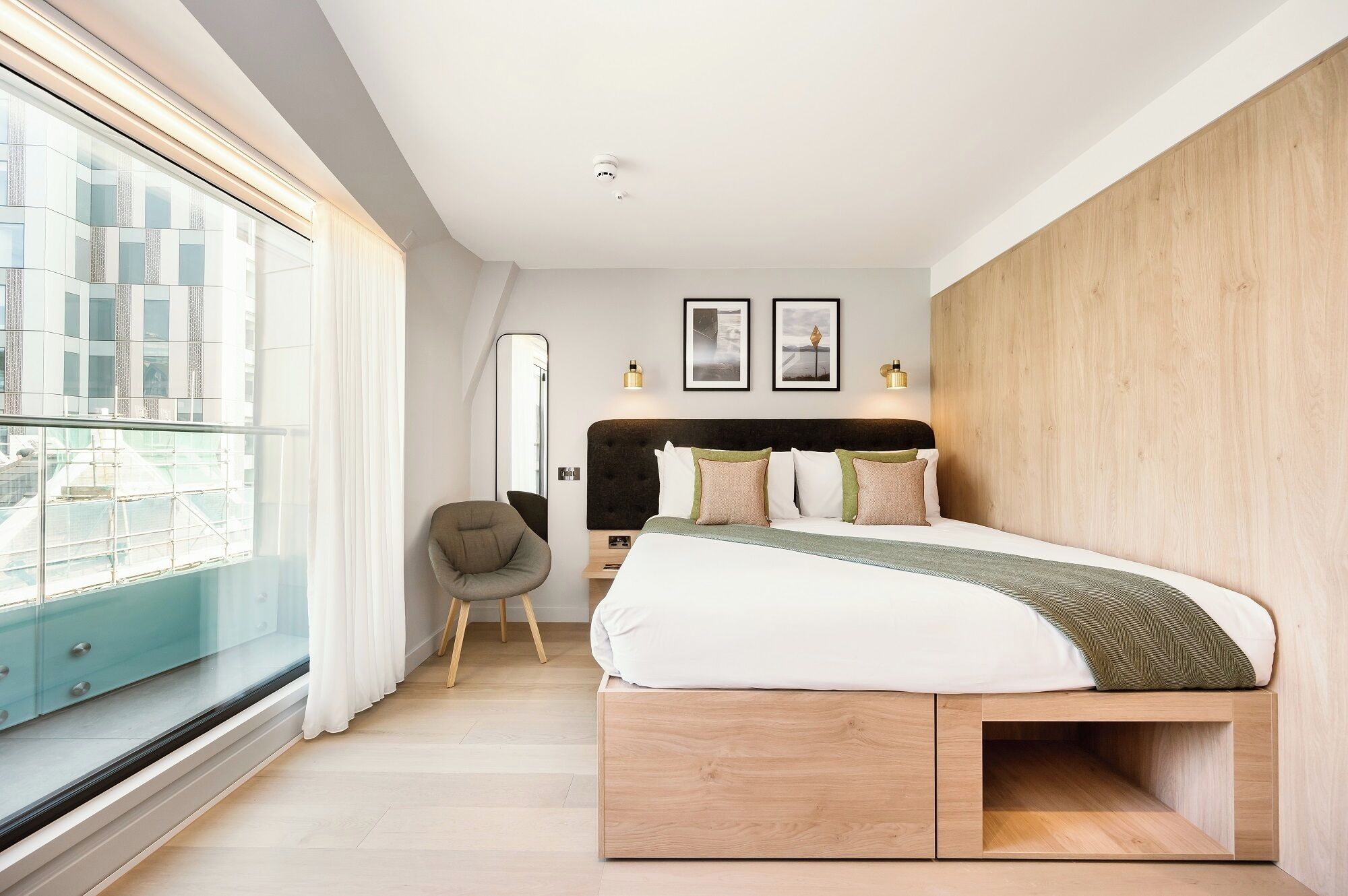 A modern bedroom with a large bed, a chair, a mirror, and artwork on the wall.