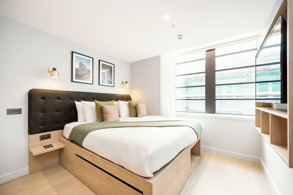 A modern bedroom with a large bed, built-in storage, a window with a view, and wall-mounted lighting.