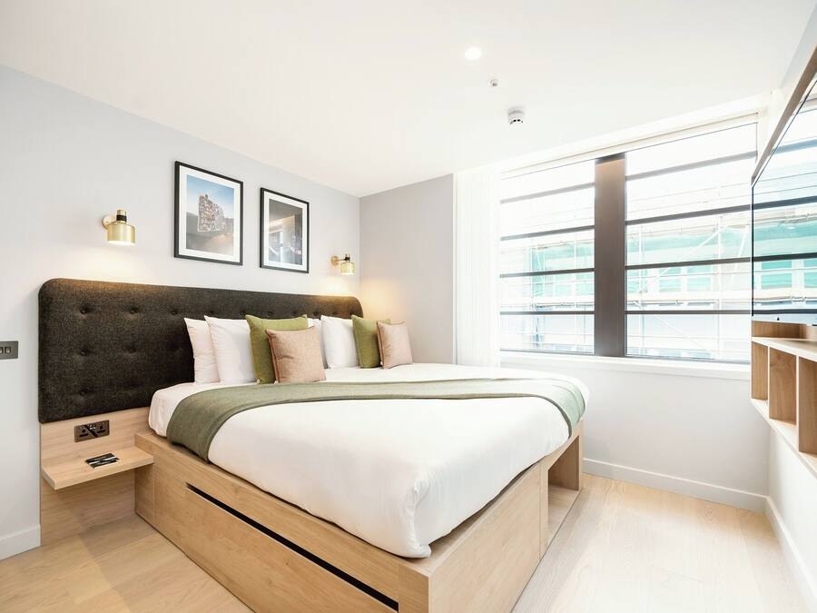 Ein modernes Schlafzimmer mit einem großen Bett, eingebauten Stauraumlösungen, einem Fenster mit Blick und Wandleuchten.
