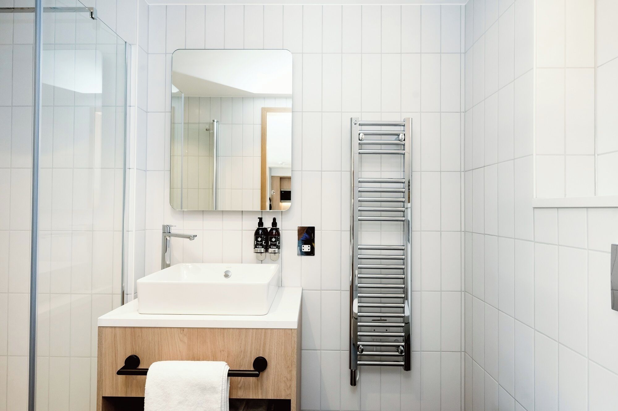 A modern bathroom with a white sink, a mirror, and a towel rack.