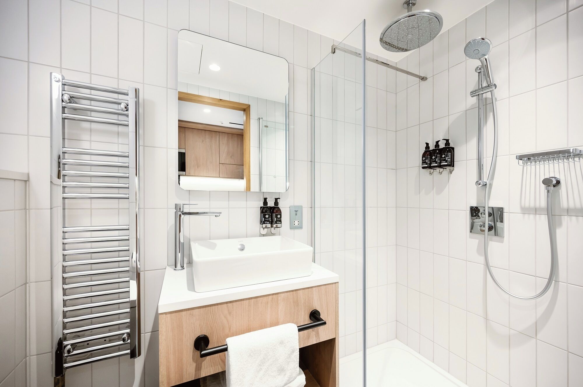 Een moderne badkamer met een douchecabine van glas, een ingebouwd wastafeltje en een handdoekrek.