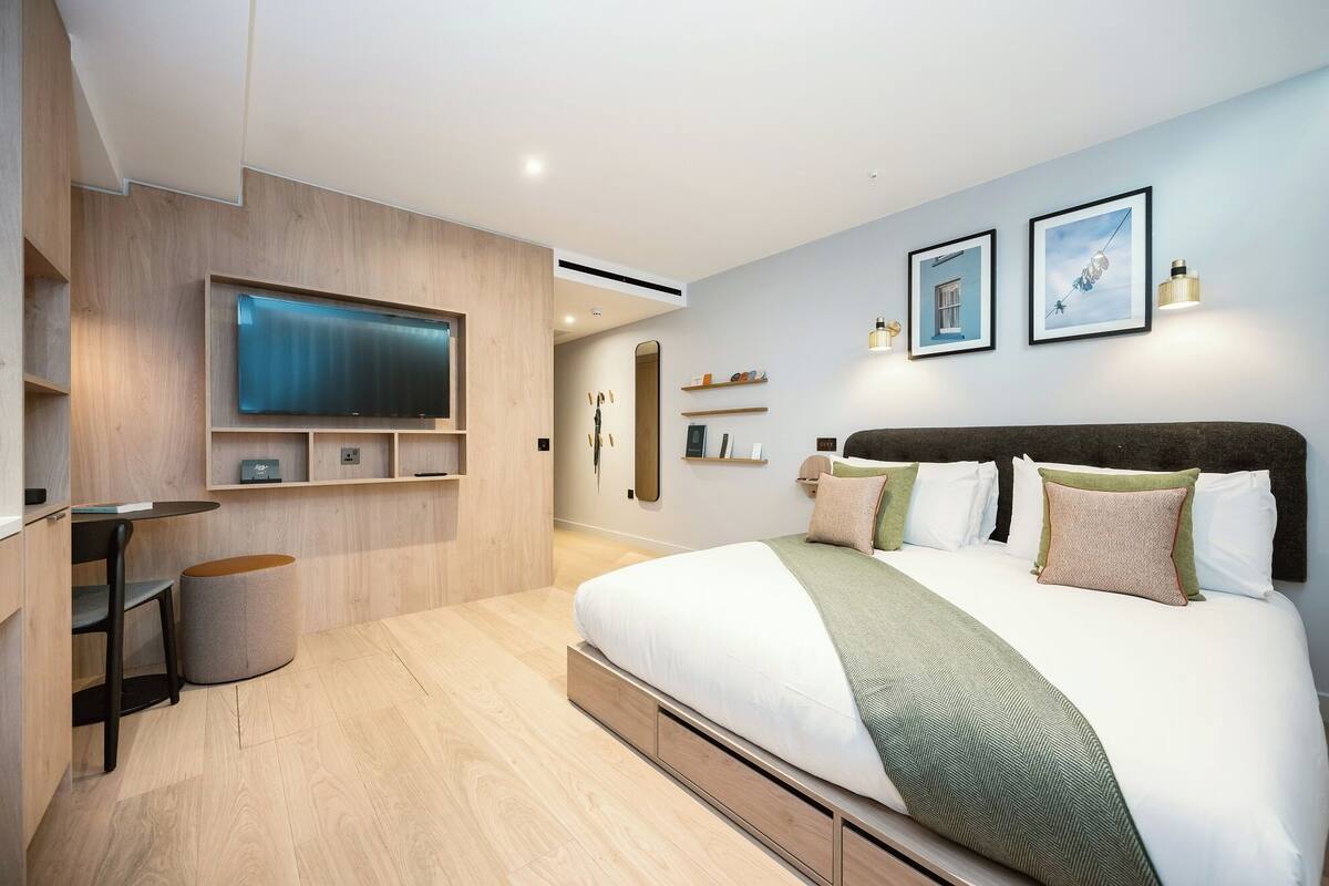 A modern bedroom with a large bed, a TV mounted on the wall, and a minimalist design.