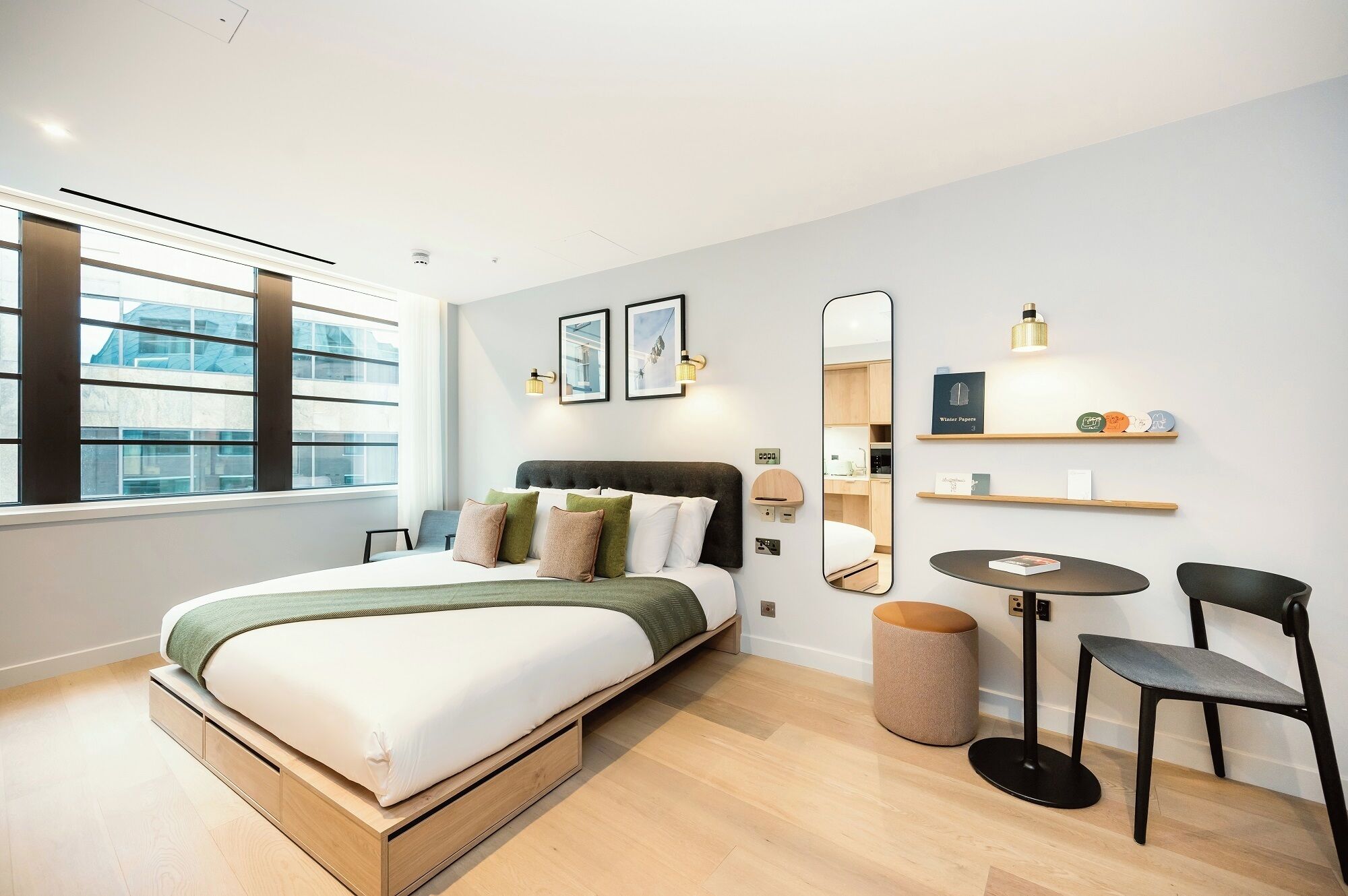 Une chambre à coucher moderne, comprenant un lit, des tables de chevet, un miroir et un petit coin salon avec une table et des chaises.