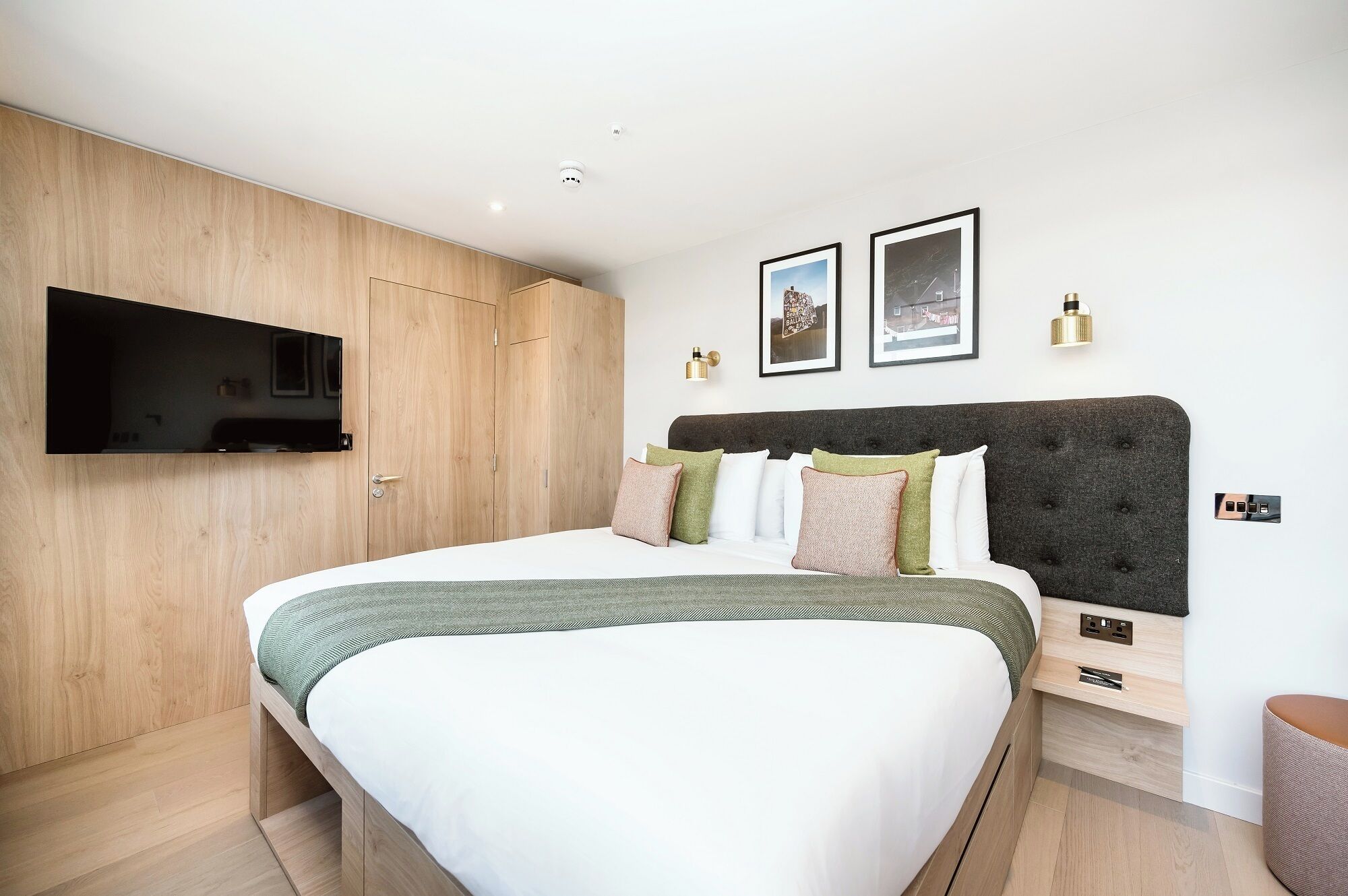 Une chambre moderne avec un grand lit, un téléviseur fixé au mur et une armoire en bois.