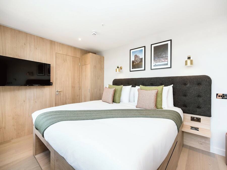 Une chambre moderne avec un grand lit, un téléviseur fixé au mur et une armoire en bois.
