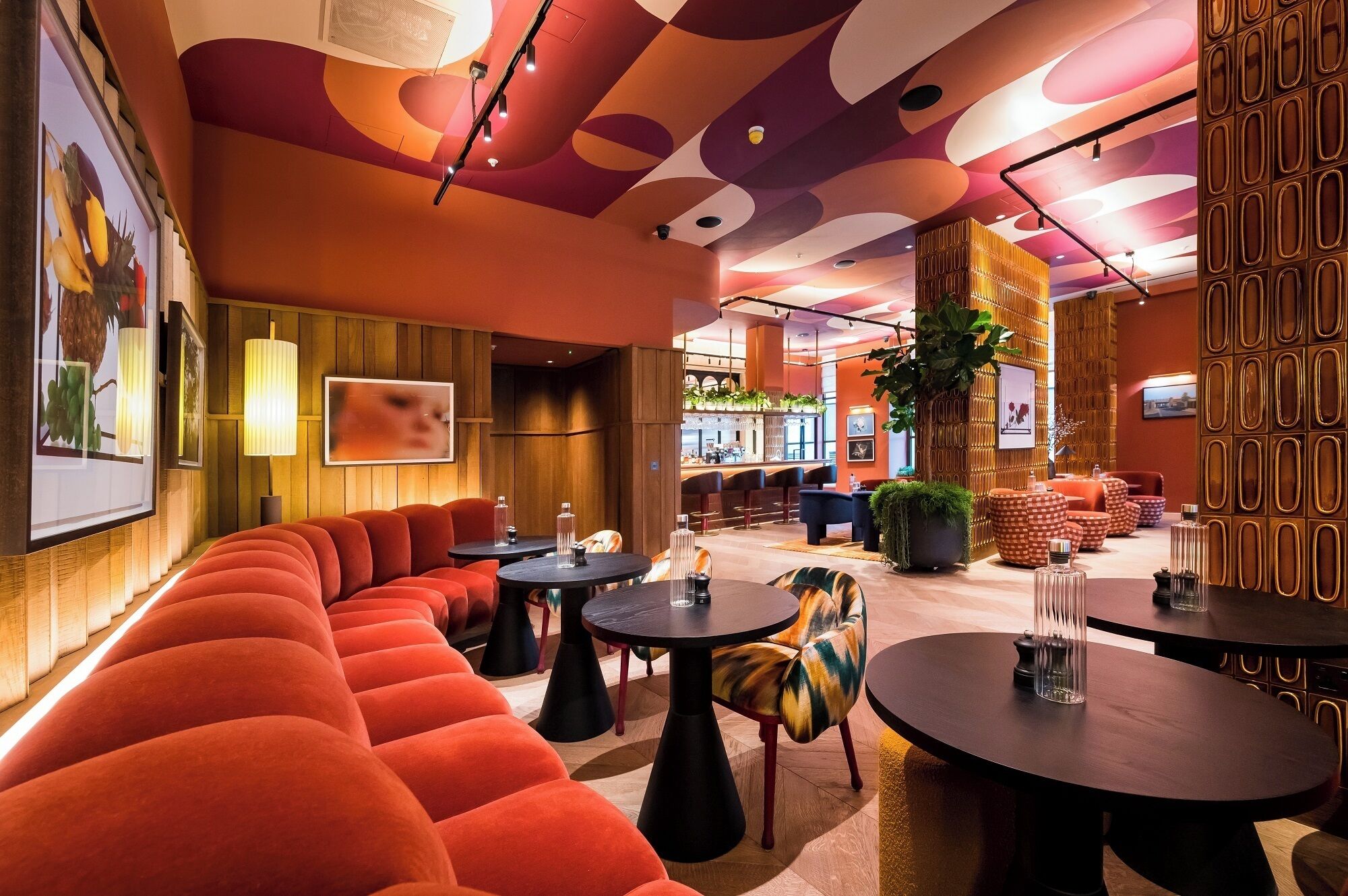 Ein moderner Lounge-Bereich mit einem gebogenen, orangefarbenen Sofa, runden Tischen und einer Bar im Hintergrund.