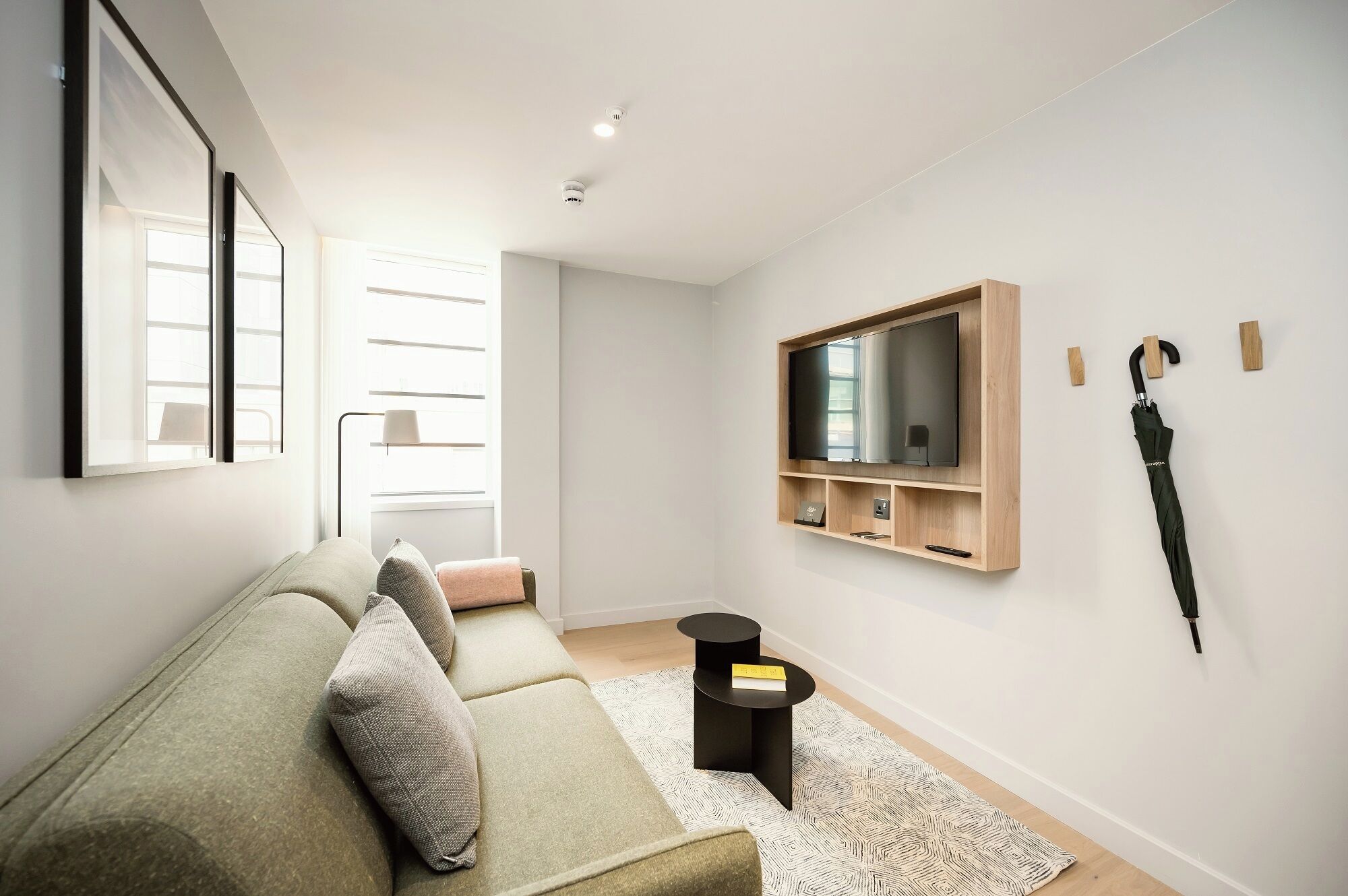 A modern living room with a green sofa, a mounted TV, a small black side table, and a patterned rug.
