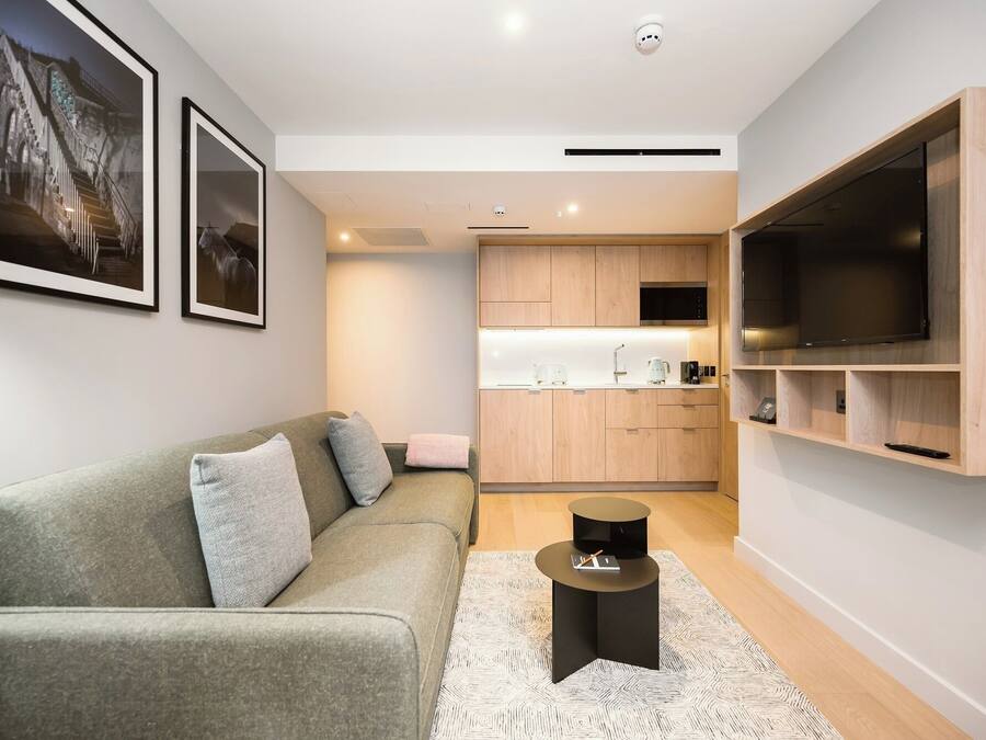 Een moderne woonkamer met een grijze bank, een zwarte salontafel en een kamerkleed met een patroon.