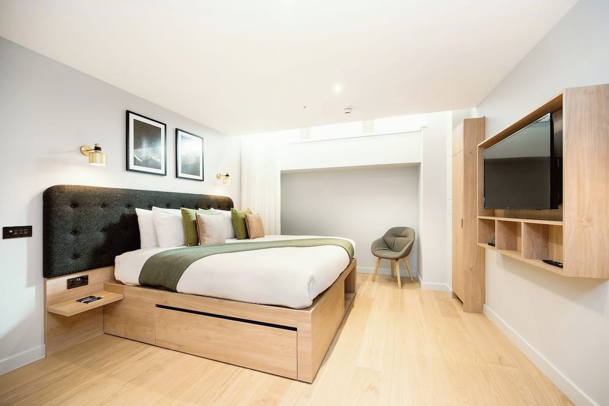 A modern bedroom with a bed, bedside tables, a chair, a TV, and a wardrobe.