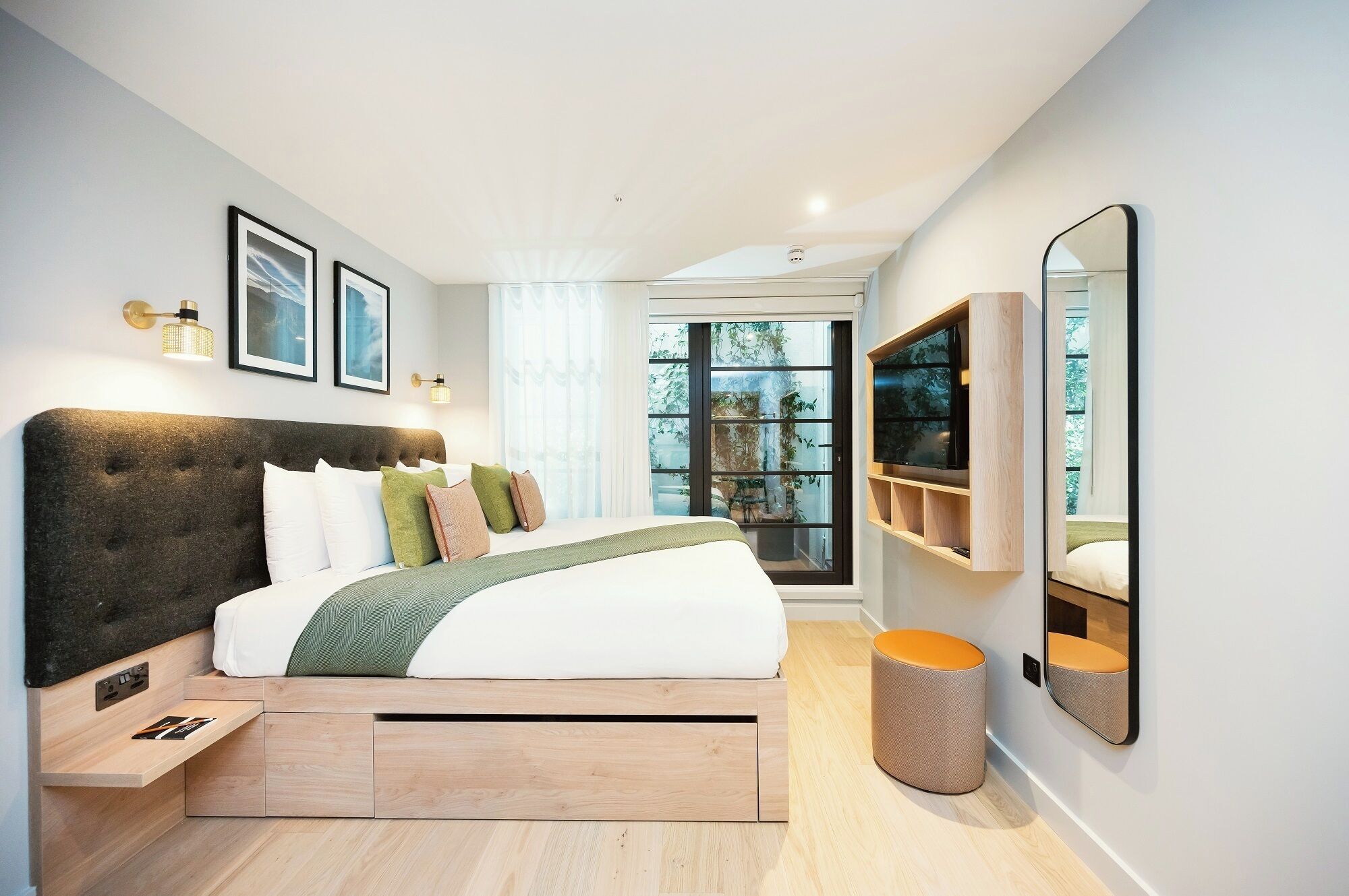 Een moderne slaapkamer met een groot bed, nachtkastjes, een televisie en een raam met uitzicht op bomen.