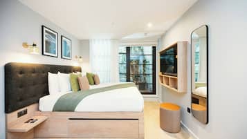 Een moderne slaapkamer met een groot bed, nachtkastjes, een televisie en een raam met uitzicht op bomen.