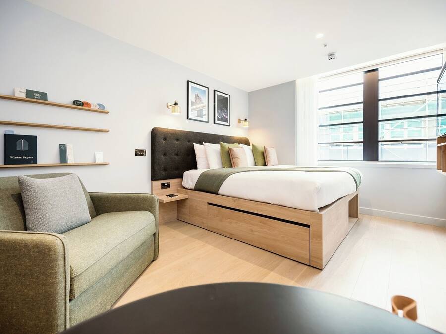 A modern bedroom with a bed, a green sofa, wooden shelves, and a large window.