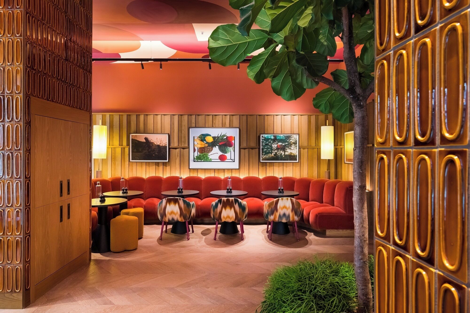 A modern lounge area with wooden paneling, red seating, and framed artwork on the walls.