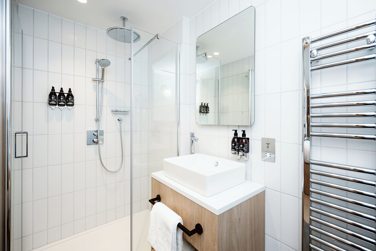 A modern bathroom with a glass-enclosed shower, a white sink, and a towel rack.