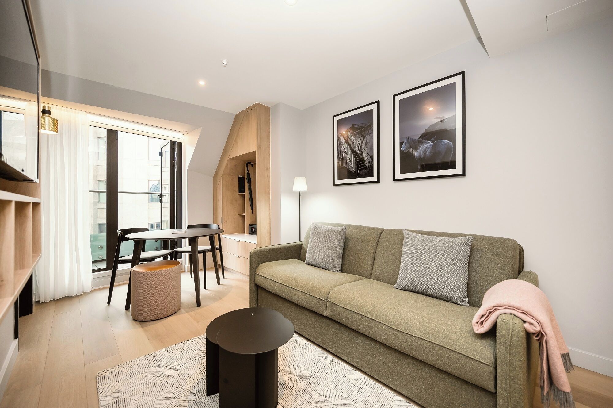 En moderne stue med sofa, sofabord og spiseplads med stole og bord. Der er to billeder i rammer på væggen.