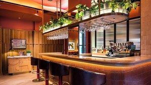 A bar area with a wooden counter, bar stools, a television screen, and potted plants. - Wilde Aparthotels London Liverpool St.  (London)