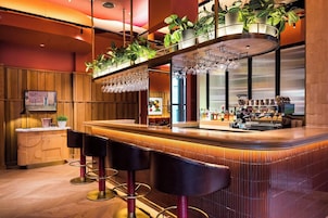 Una zona de bar con mostrador de madera, taburetes, una pantalla de televisión y plantas en macetas.