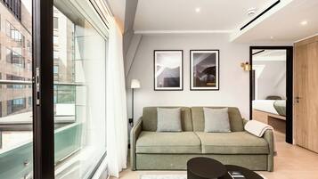 A modern living room with a green sofa, two framed pictures on the wall, a small table, and a large window.