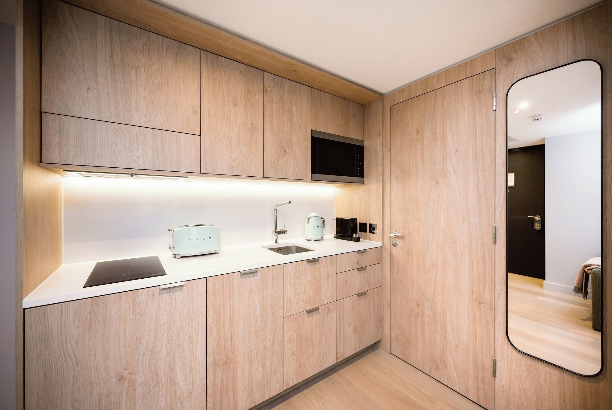 A modern kitchen with wooden cabinets, a white countertop, a toaster, a kettle, and a black microwave.