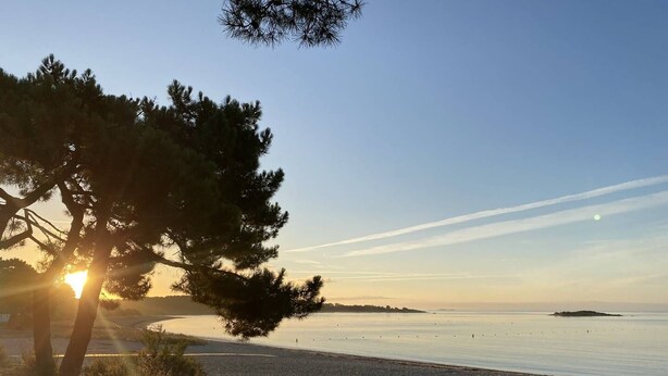 Une plage avec un ciel dégagé, un coucher de soleil et une île lointaine.