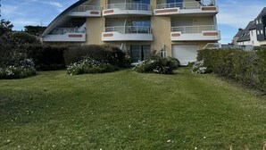 Un immeuble résidentiel à plusieurs étages, doté de balcons, d’un toit en pente et d’une pelouse bien entretenue.