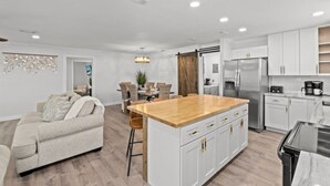 A modern kitchen with white cabinets, a wooden island, stainless steel appliances, and a dining area with a table and chairs.